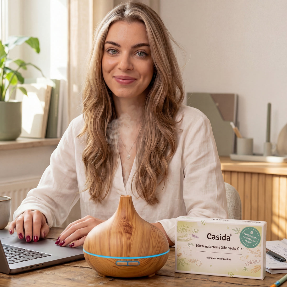 Frau am Laptop neben Casida Duftdiffuser in Holzoptik und Duftmischungen-Set.