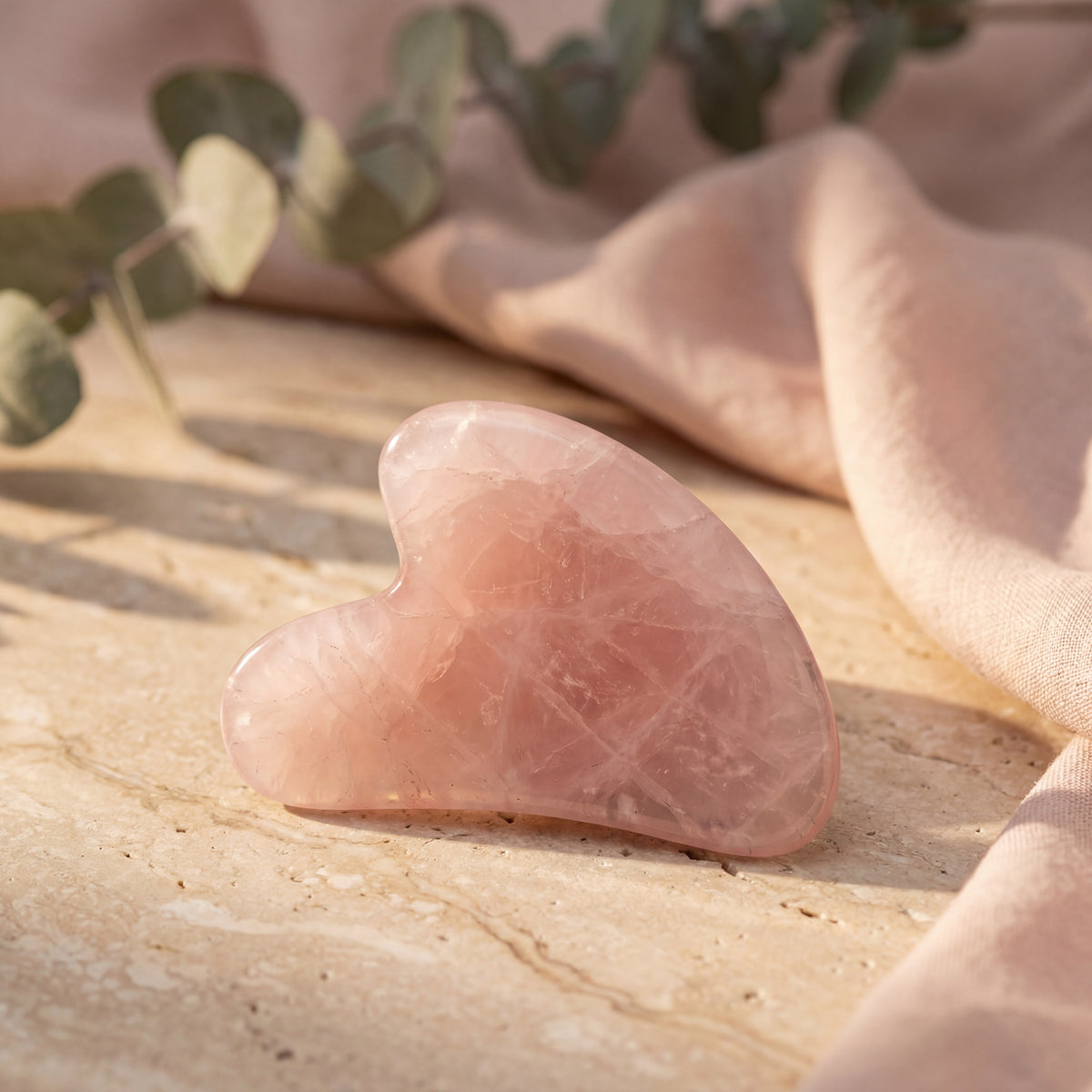 Rosafarbener Gua-Sha-Stein in Herzform auf einer Steinfläche neben einem Tuch