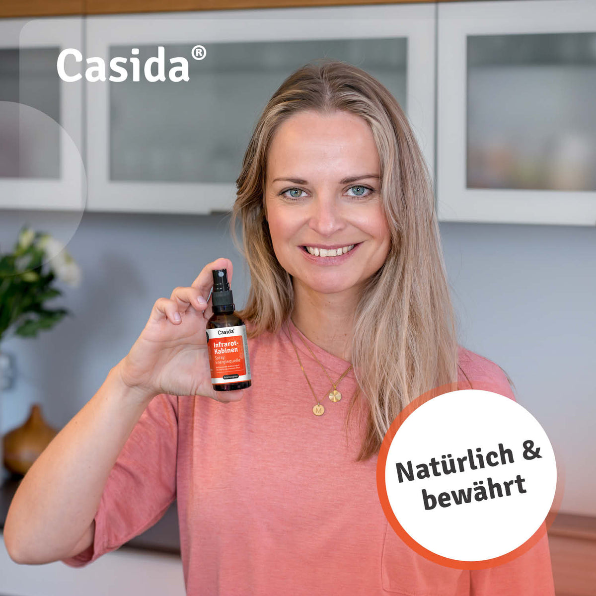 Casida infrarotkabinen spray held by a woman in a pink shirt, with a modern kitchen background.
