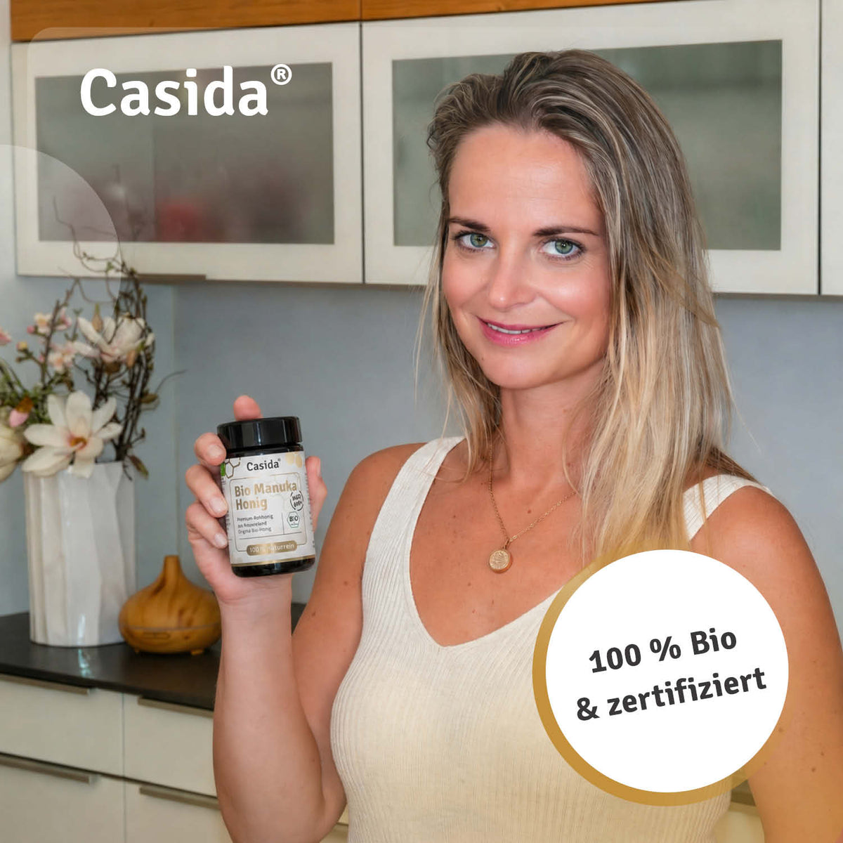 Casida Bio Manuka honey MGO 600+ in a small jar held by a woman in a kitchen setting.