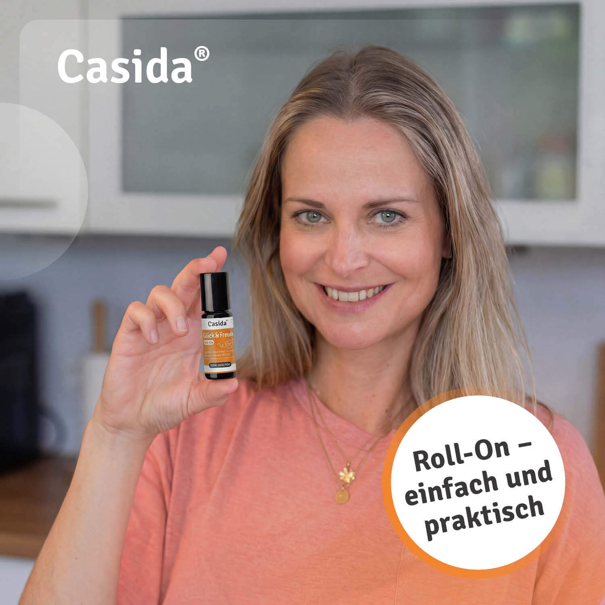 Glück & Freude roll-on for good mood held by a woman in a pink shirt, with a kitchen background.