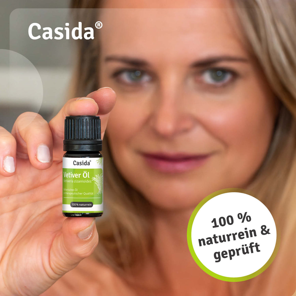 Casida vetiver oil bottle held by a woman, featuring a green label and black cap, with a blurred background.