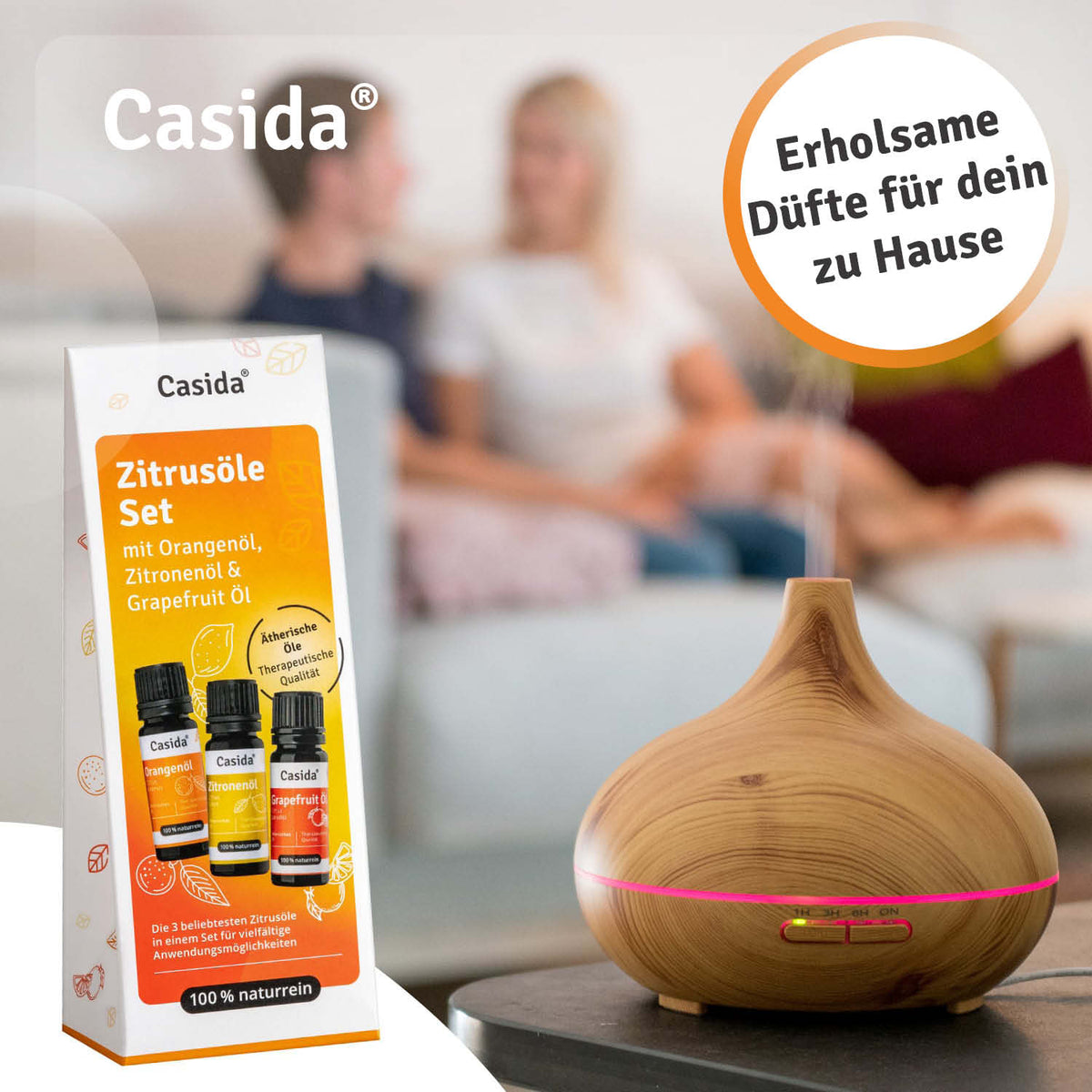 Casida Zitrusöle-Set neben einem Diffuser in Holzoptik, im Hintergrund ein Paar auf dem Sofa