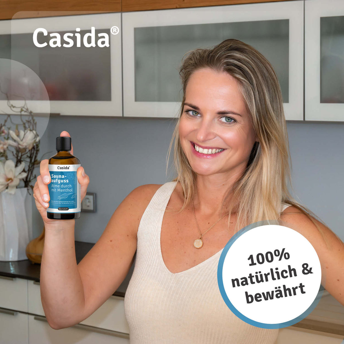 Casida saunaaufguss Atme durch mit Menthol oil in a woman's hand, smiling in a modern kitchen setting.