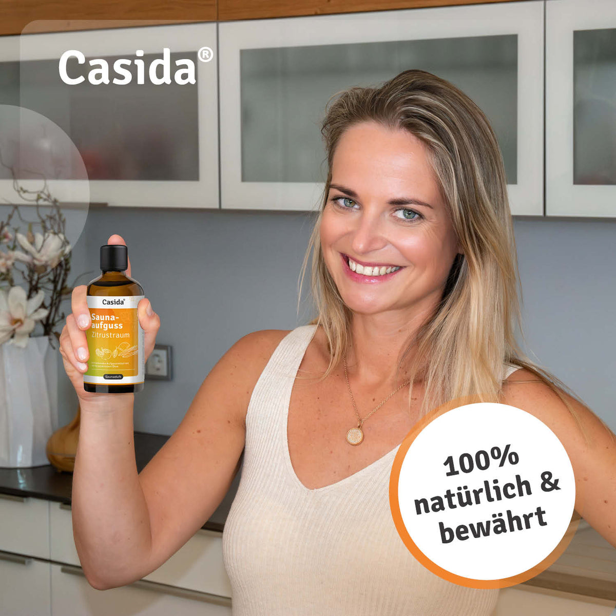 Saunaaufguss Zitrustraum oil in a bottle held by a smiling woman in a kitchen setting.